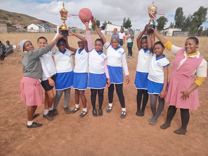 Victory learners holding two trophies and a ball high above their heads on the sports field